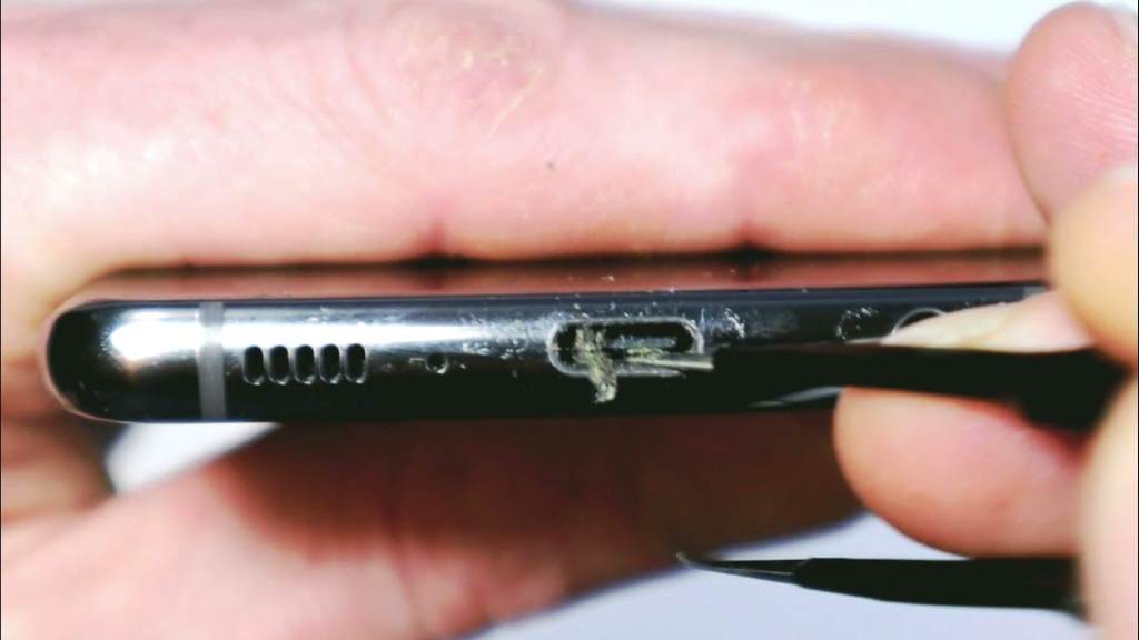Person cleaning a laptop charging port with a soft brush to remove debris.
